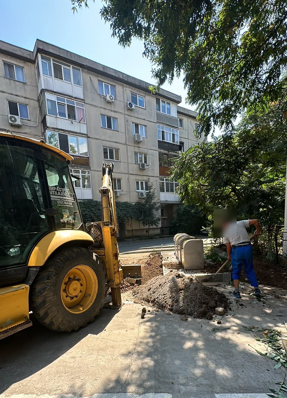 Buldoexcavator Impact Utilaje lângă containere de gunoi semi-îngropate nou montate în curtea unui bloc