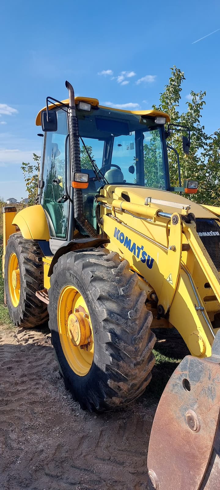 Cabina și brațul încărcătorului unui buldoexcavator Komatsu galben, în lumina după-amiezii