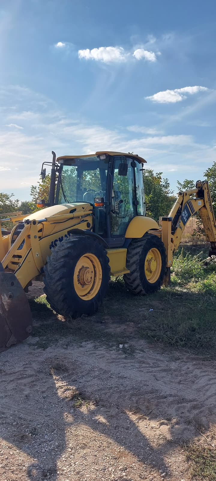 Buldoexcavator Komatsu WB93S parcat pe un teren de pământ, într-o zi însorită