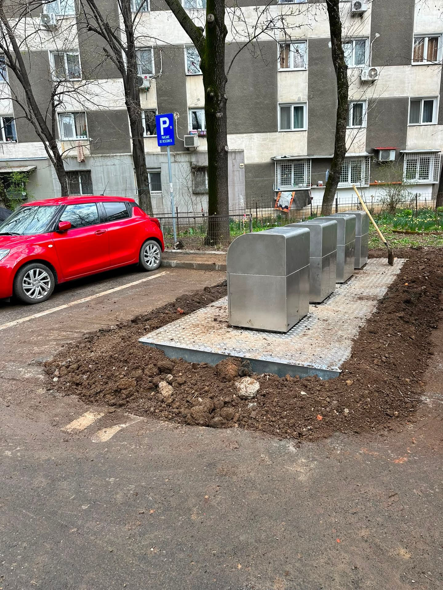 Platformă cu containere îngropate din inox montată în parcarea unui bloc, cu pământ proaspăt săpat în jur